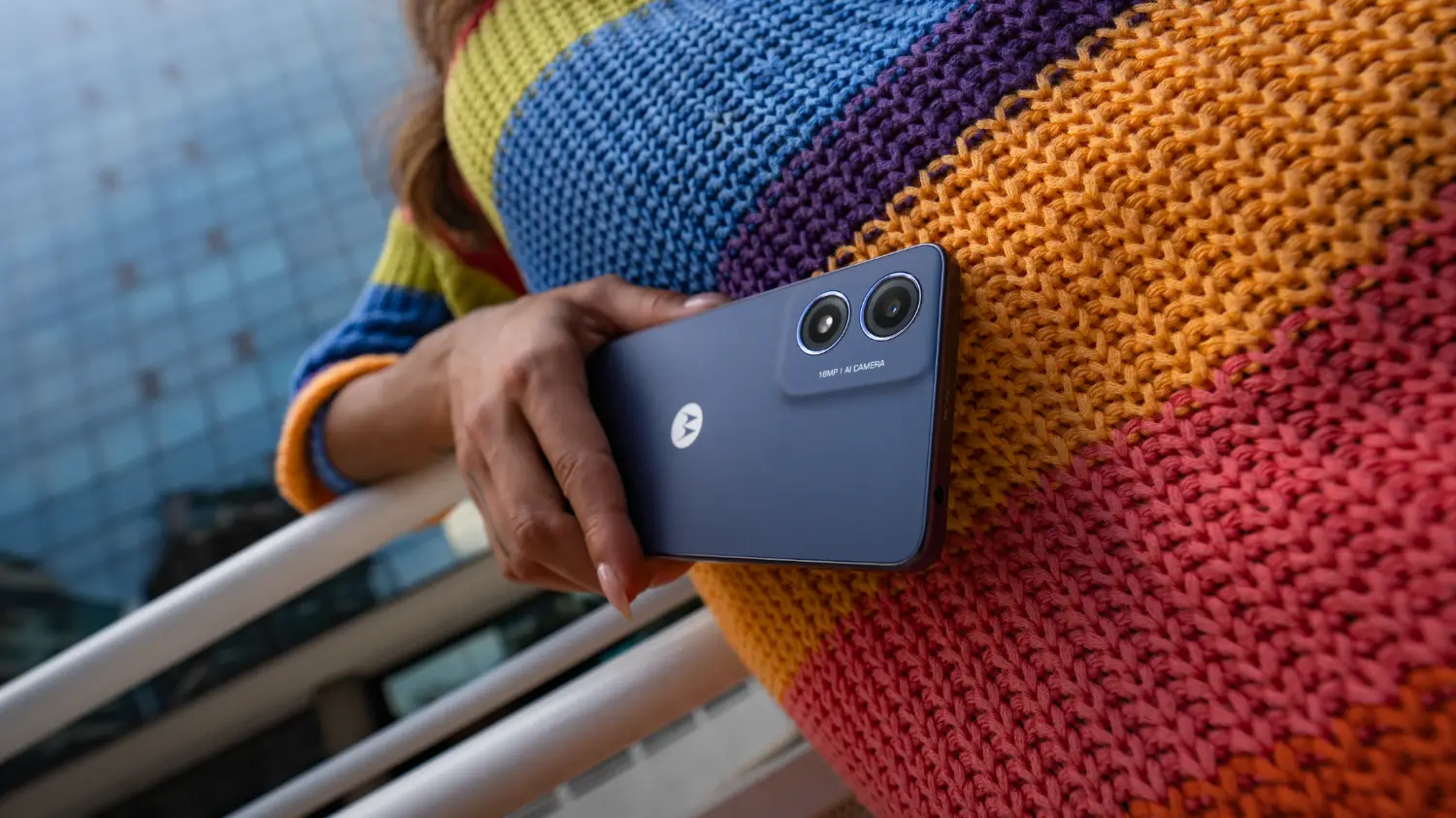 The budget Moto G04 being held in front of a colourful knitted sweater