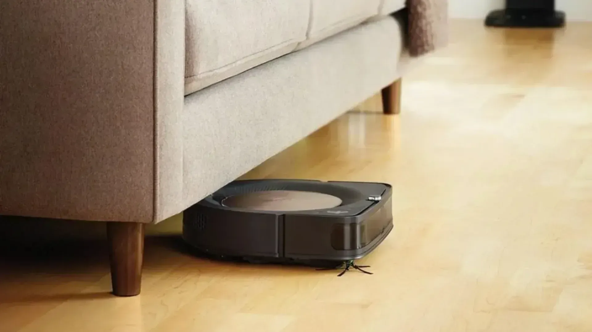 The iRobot Roomba S9+ vacuuming under a lounge on a wooden floor