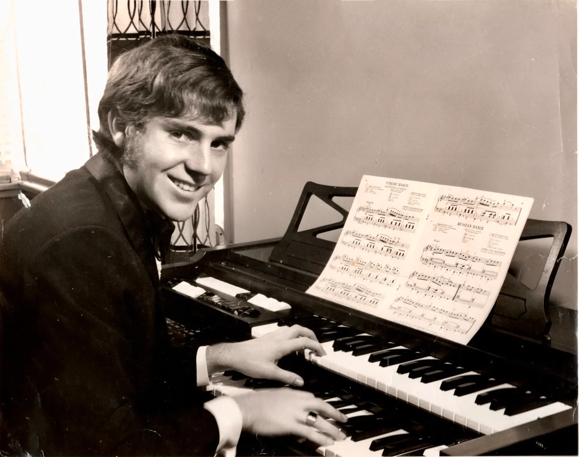 An old sepia photo of my dad playing an organ, smiling to the camera