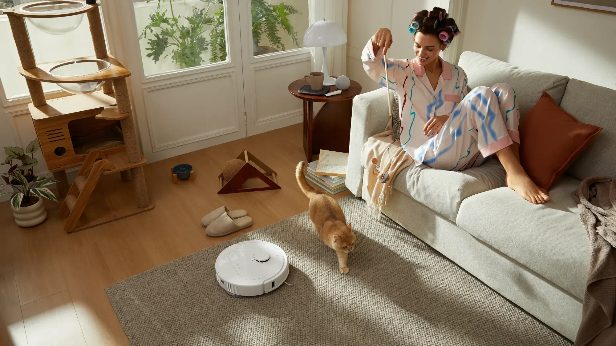 A woman on a lounge with ethe Qrevo S cleaning a carpet next to a cat