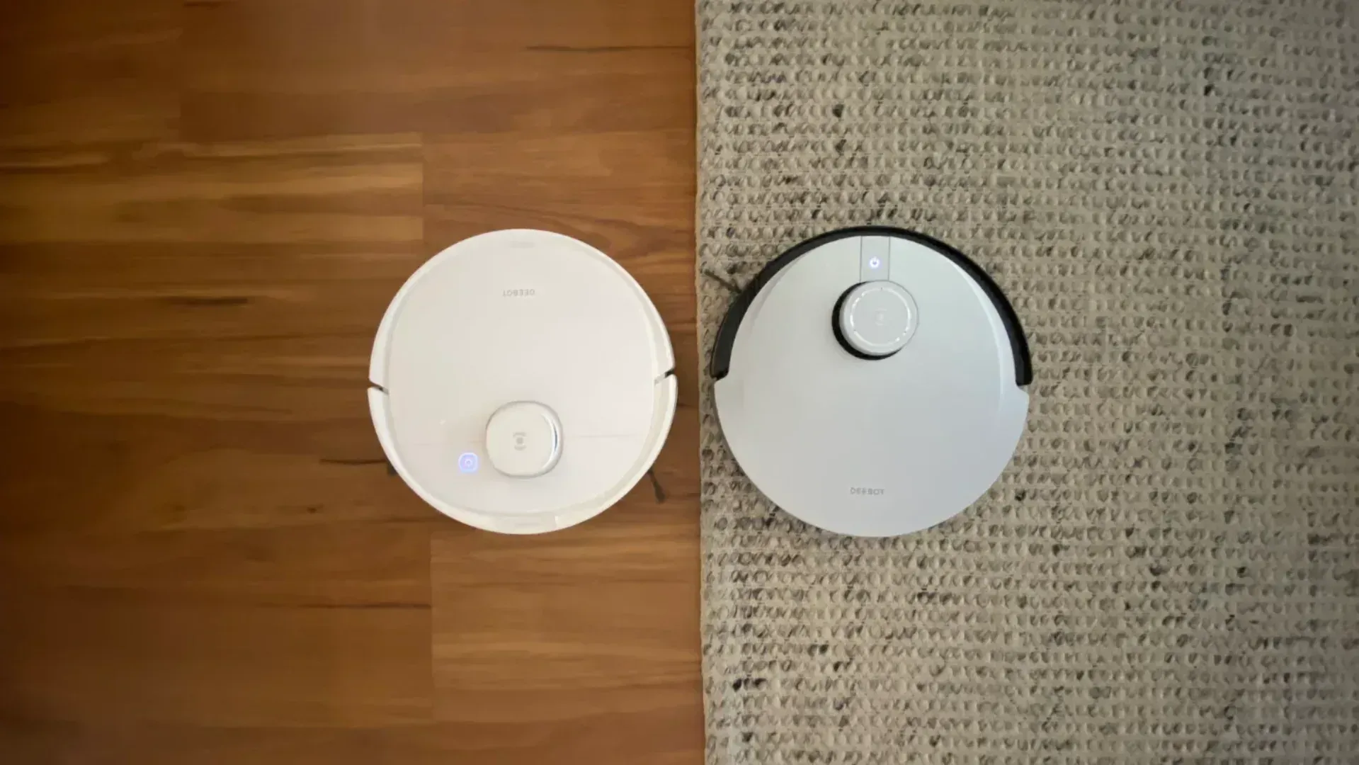 Two robot vacuums side by side, one on hard floor, one on a rug.