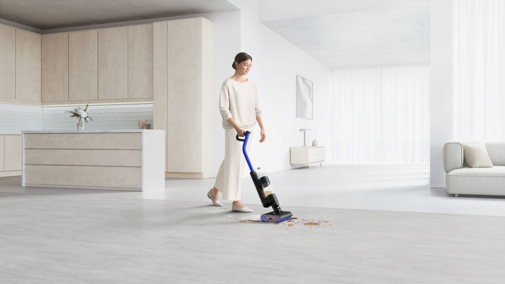 A woman in a white room using the Dyson WashG1 to clean up mess on the floor