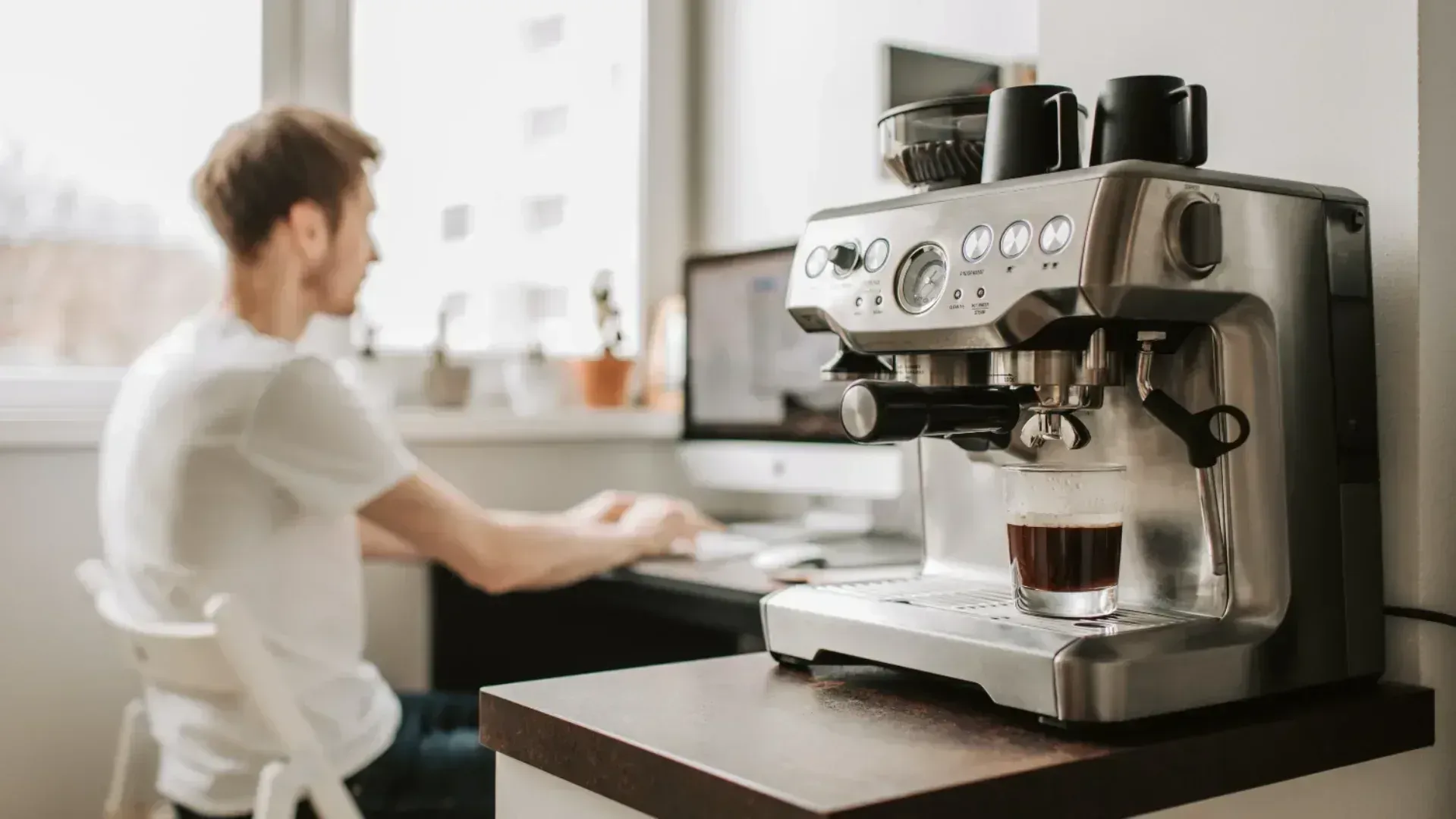 A man working in the background while an espresso machine makes a coffee.