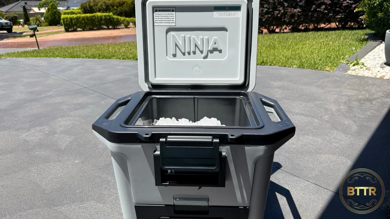 The Ninja FrostVault 28 Litre, sitting on a driveway with the lid open and full of ice.