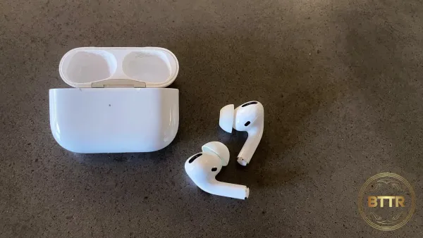 The Airpods Pro case and the earbuds sitting loose next to the case on a concrete table