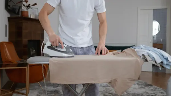 A man ironing his shirt on an ironing board