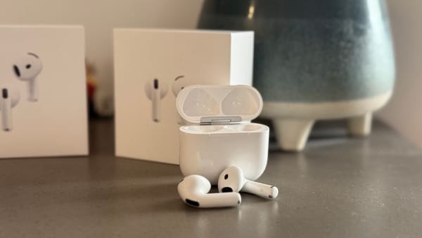 The AirPods 4 in front of their case on a concrete bench in front of a pot plant