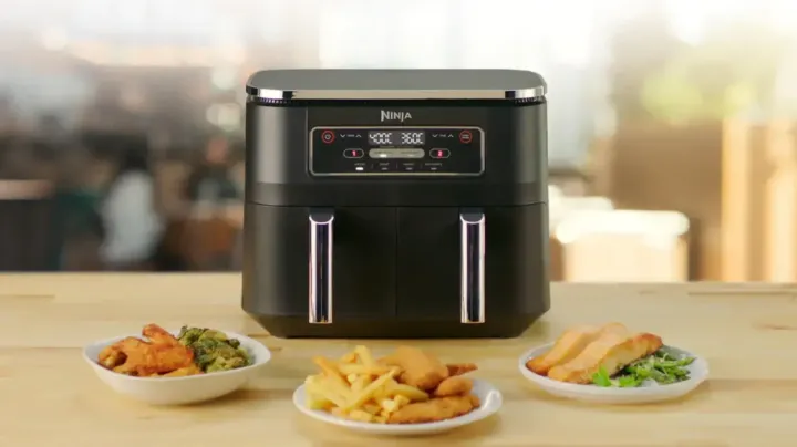 A Ninja air fryer on a bench with three plates of food in front