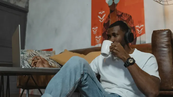 Man drinking coffee while using his computer and listening to a pair of wireless headphones