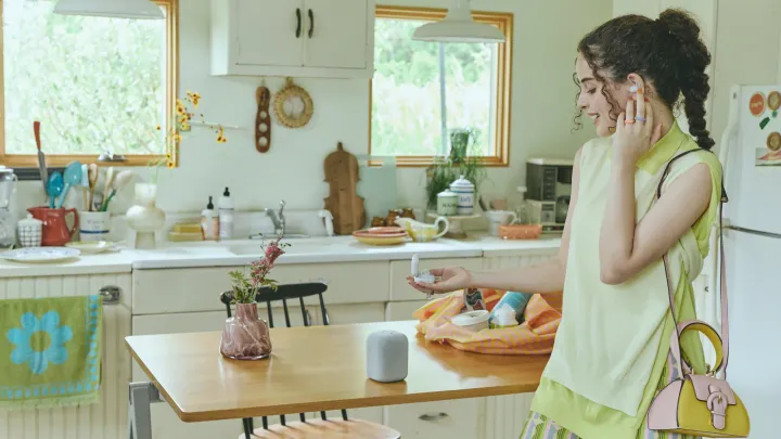 A woman in a green kitchen transferring music from her LinkBuds to the LinkBuds speaker